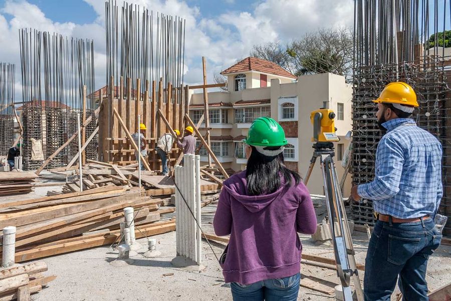Two members of the firm beside the theodolite, in front of the column rebar cages on a construction site