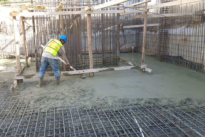 A worker levels freshly poured concrete over the steel rebar mat