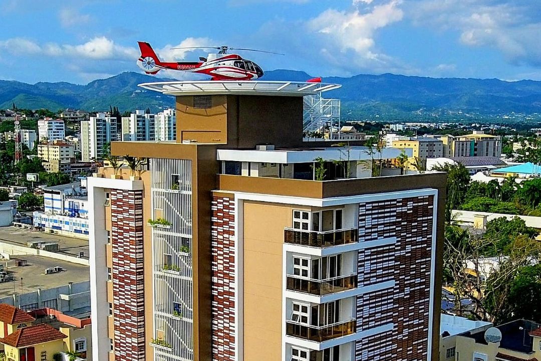 Sommet d’une tour résidentielle doté d’un héliport où est posé un hélicoptère, la ville et la montagne en arrière-plan